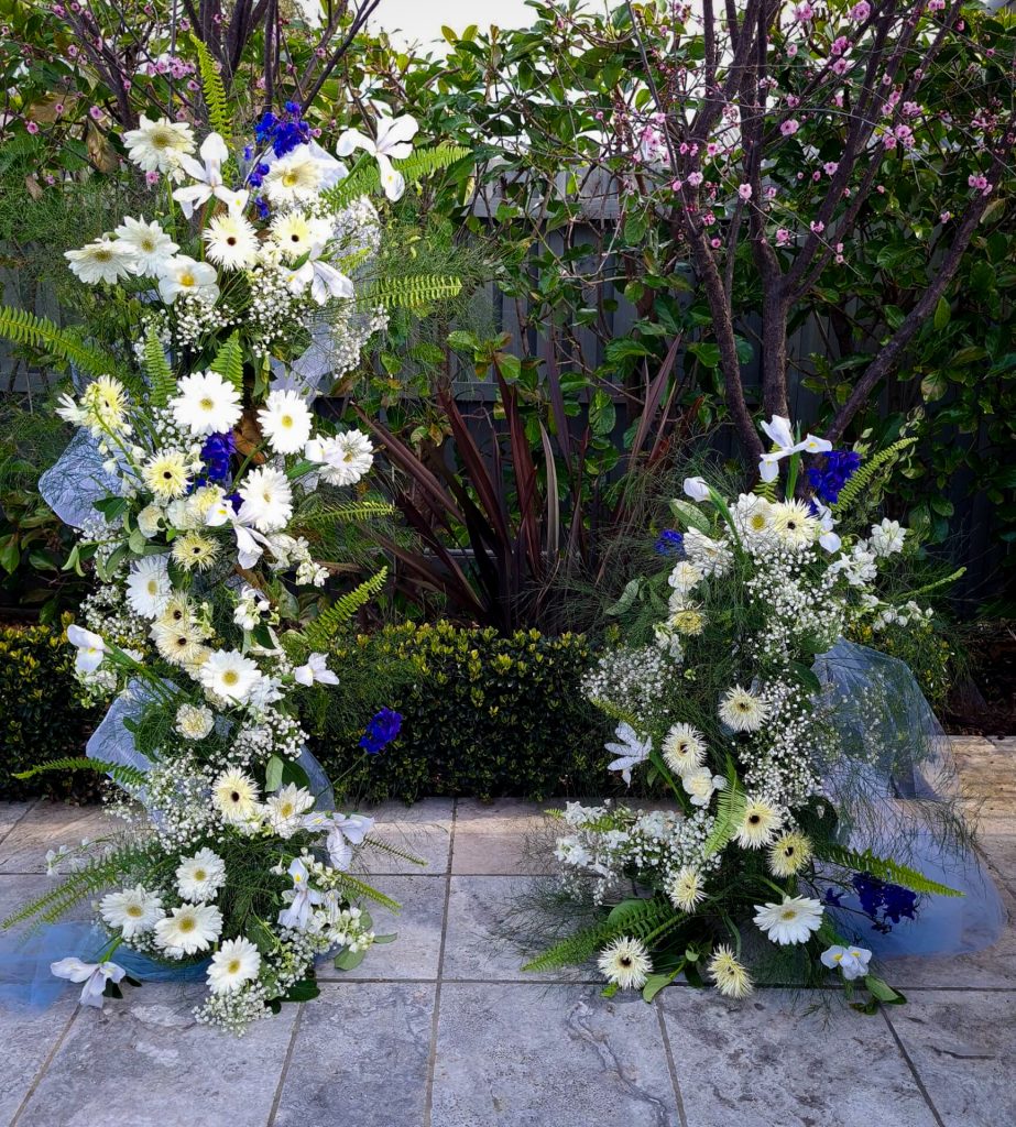 Wedding flower towers for ceremony installation with white gerberas, gypsophila, white and blue irises, green fern foliage woven with light blue organza