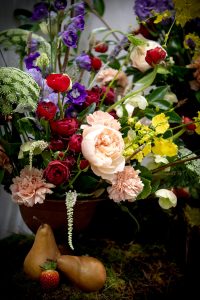 Abundant wedding copper compote with Queen Anne's lace, red spray roses, peach garden roses, peach carnations, dancing lady orchids, green hellebores, and purple and lilac delphinium