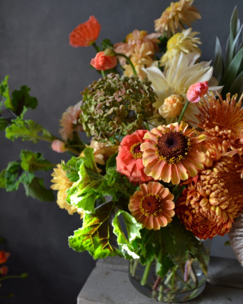 A close up of a vase of flowers. Orange zinnia, chrysanthemums and lemon dahlia