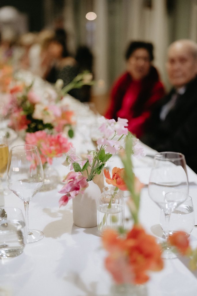 Close up of small bud vase flowers on a dinning table. Flowers are pink and orange