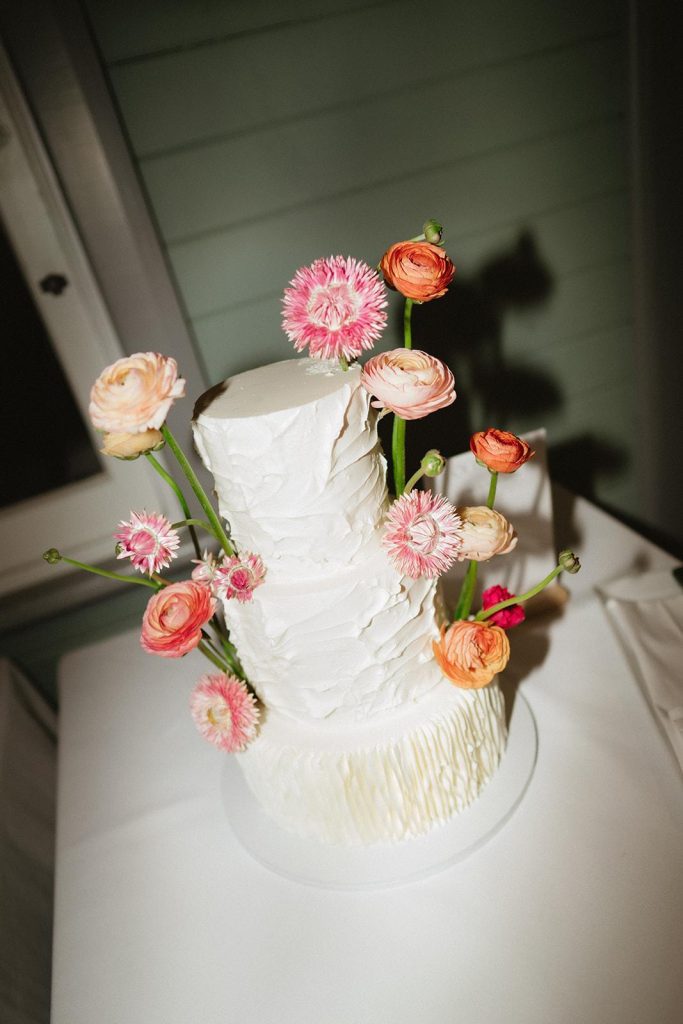 2 tiered white wedding cake with pink and orange floral decorations