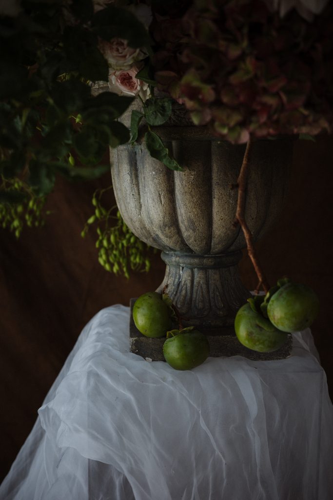 Close up of grey urn with green fruit scattered around the base