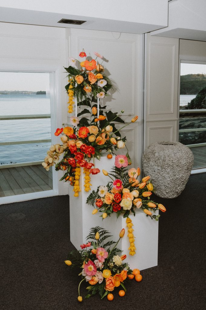 Close up of yellow and orange florals arranged in a sculptural design on 2 white plinths