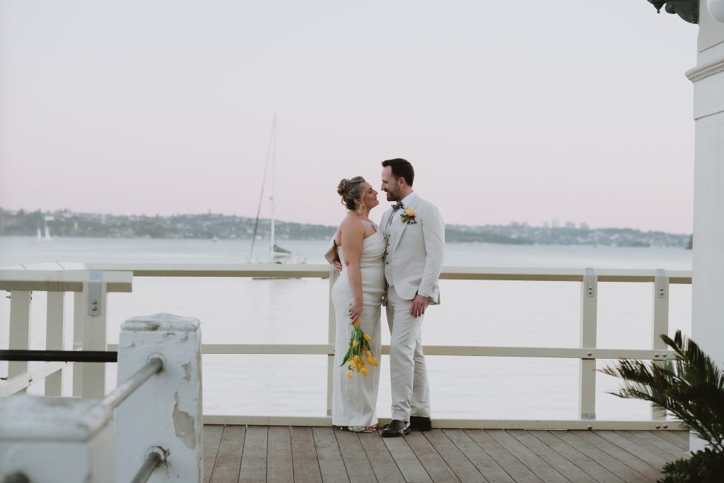 A wedding couple stand at the end of a boardwalk, overlooking the ocean